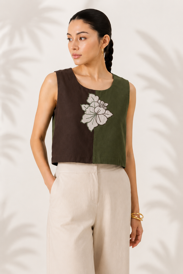 A woman modeling a sleeveless crop top with a split design: dark brown on the left and olive green on the right, featuring a  floral motif patch embroidery.