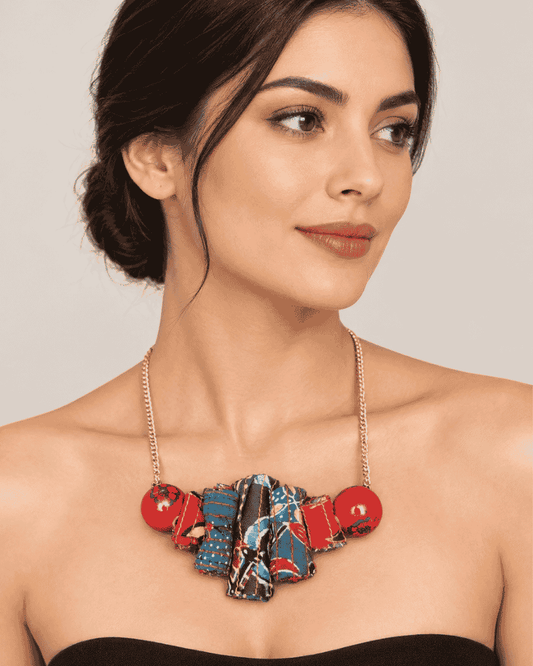 Woman wearing a handcrafted statement necklace featuring red circular accents and a blue textile centerpiece.
