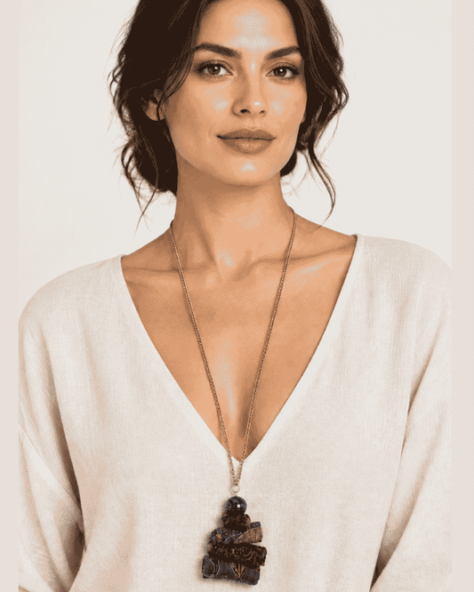 Woman wearing a long necklace with a dark blue statement pendant and a white V-neck top.
