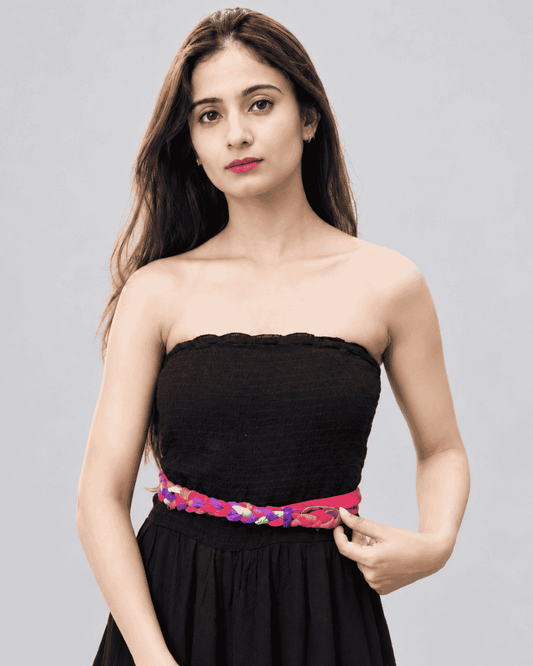 Woman wearing a pink braided waist belt with a black strapless dress.
