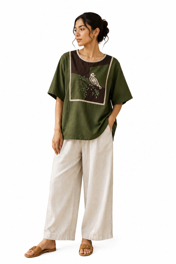Maira green cotton top with a contrasting brown front panel and handcrafted bird-and-branch motif, modeled by a woman.
