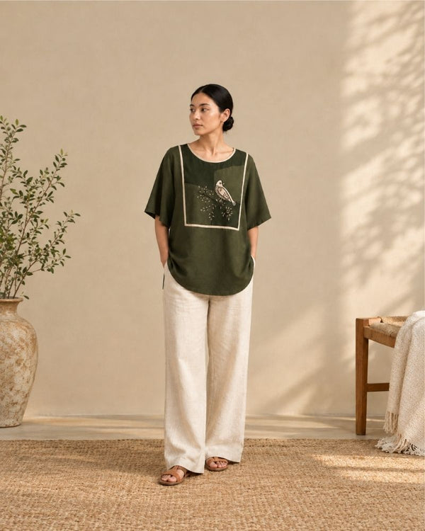 Woman wearing the dark green Maira Top with white trousers, showcasing its relaxed fit and three-quarter sleeves by Bunko Junko.