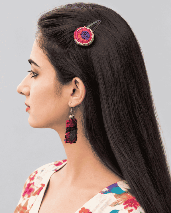 Woman wearing a handcrafted round pink and red spiral hair pin in her long dark hair.
