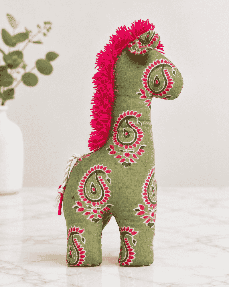 Green paisley fabric horse plush toy with a pink fringe mane standing on a marble surface