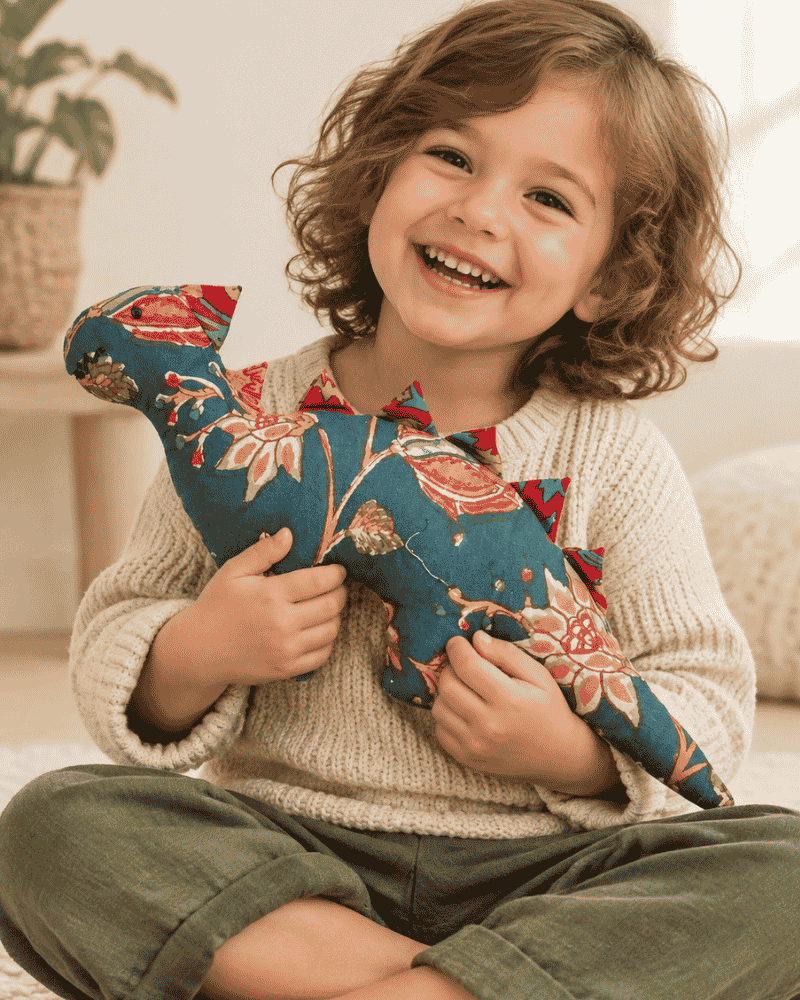 Smiling child hugging a teal floral dinosaur soft toy with red fabric spikes.