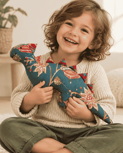 Smiling child hugging a teal floral dinosaur soft toy with red fabric spikes.