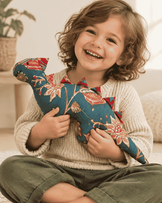 Smiling child hugging a teal floral dinosaur soft toy with red fabric spikes.