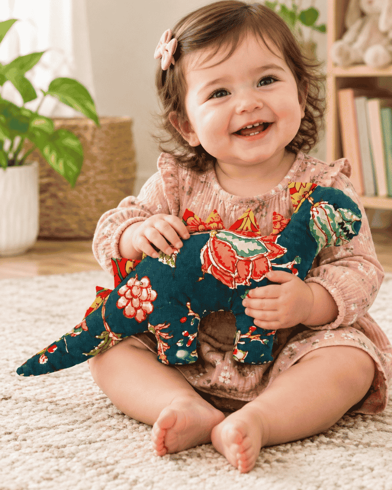 Seated child holding a teal floral dinosaur soft toy across their lap.