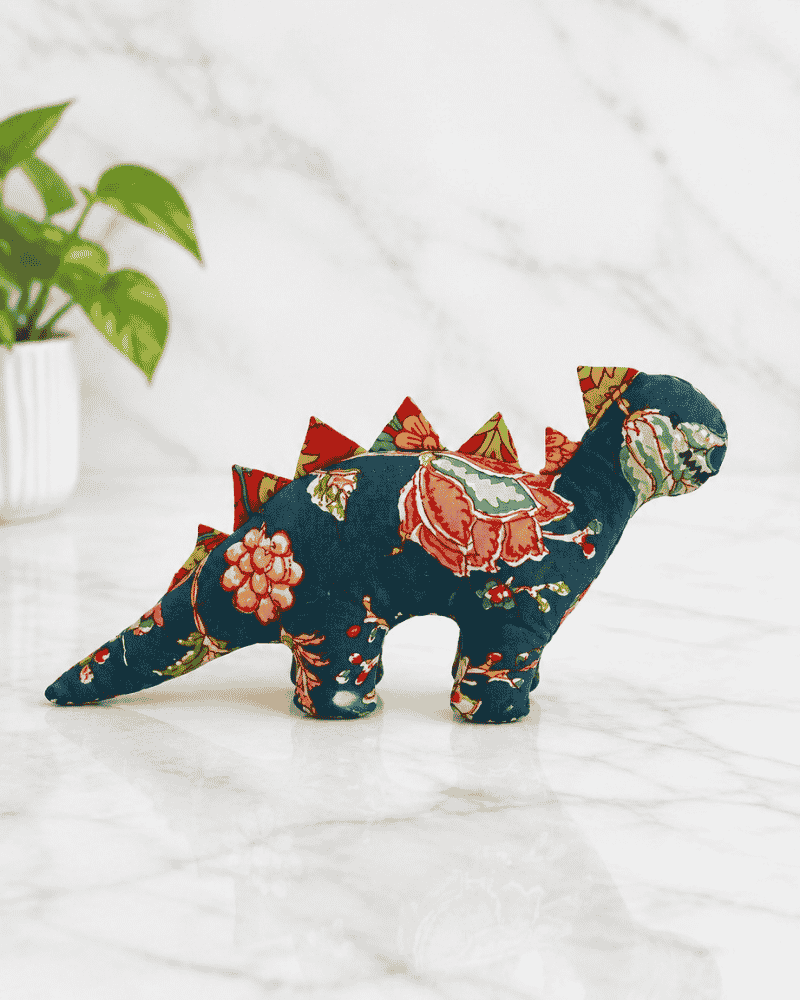 Side view of a teal floral dinosaur soft toy with red triangular spikes and a long tail.