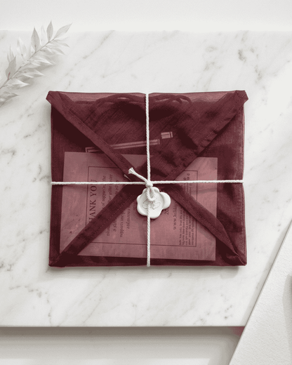 Burgundy fabric envelope with white cord tie and decorative charm